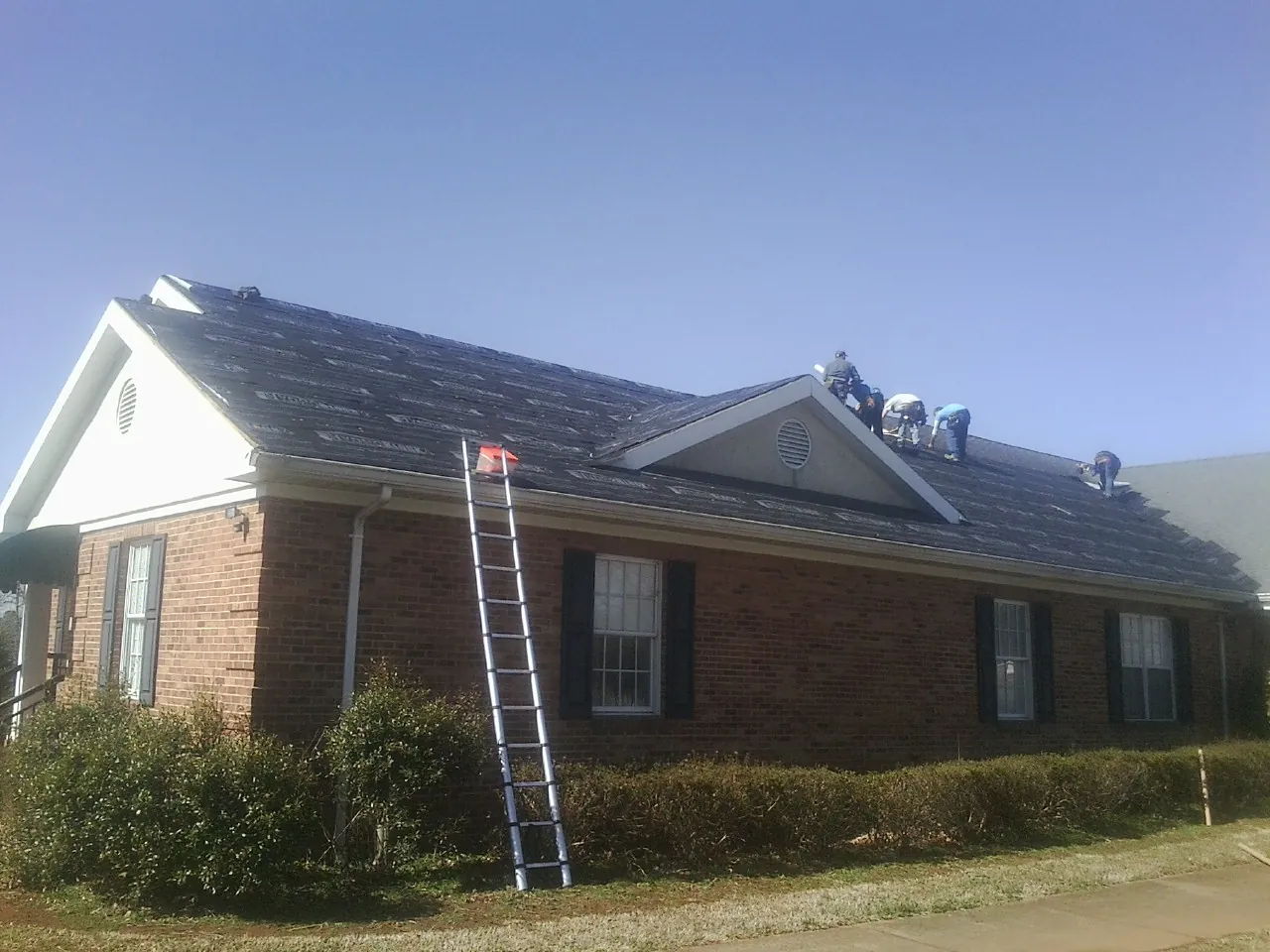 Crew tearing shingles off a brick ranch roof with a ladder set — Emergency Roof Repair work by our crew in Tobyhanna