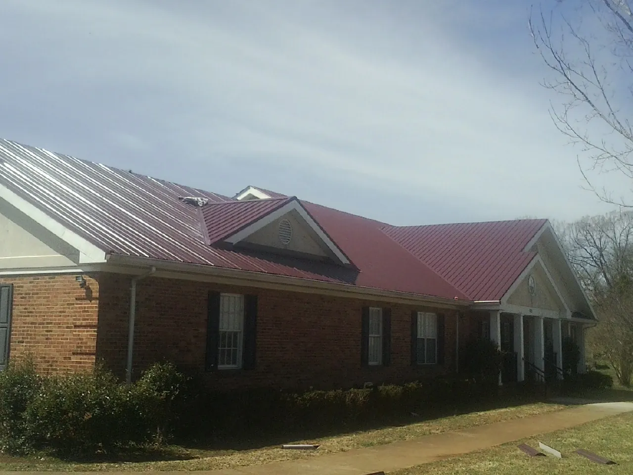 Red metal roof with gabled entries on a long brick building, from a Hail Damage Roof Repair job in Tobyhanna