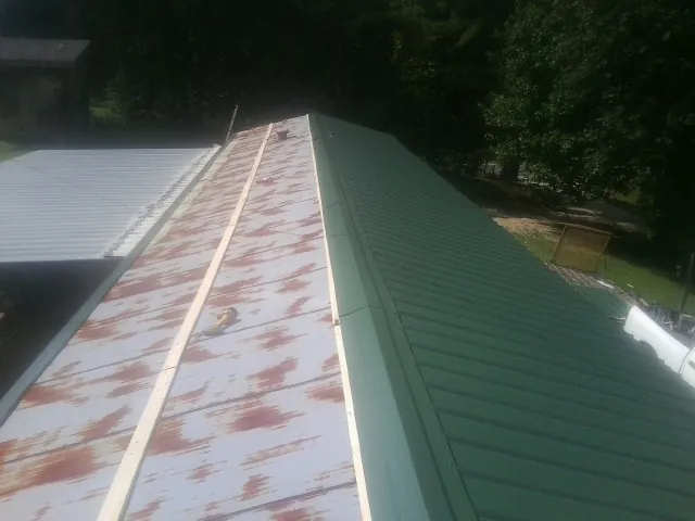 Old rusted panels beside newly installed green metal roofing — Wind Damage Roof Repair by Roofing Brothers in Tobyhanna