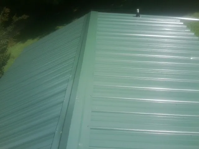 New green metal panels meeting at the ridge of a roof — Flat Roof Repair work by our crew in Tobyhanna