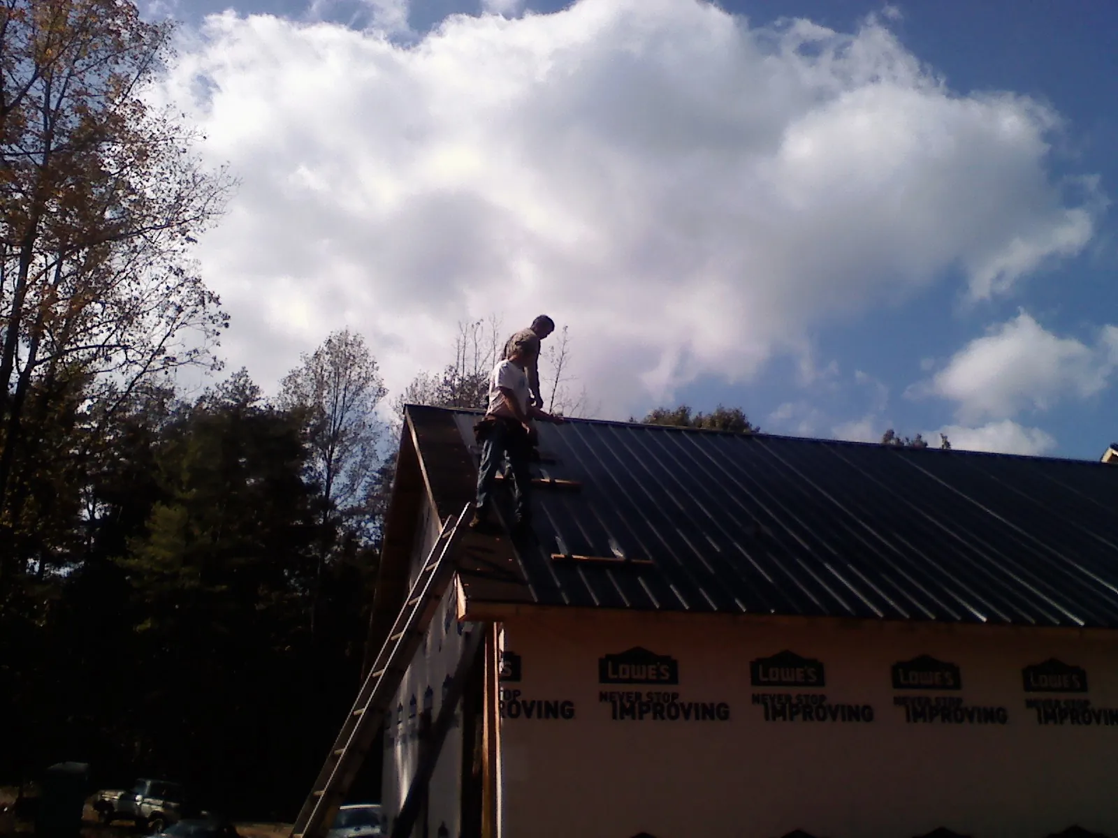 Roofer fastening dark metal panels high against a cloudy sky, from a Roof Inspection job in Tobyhanna