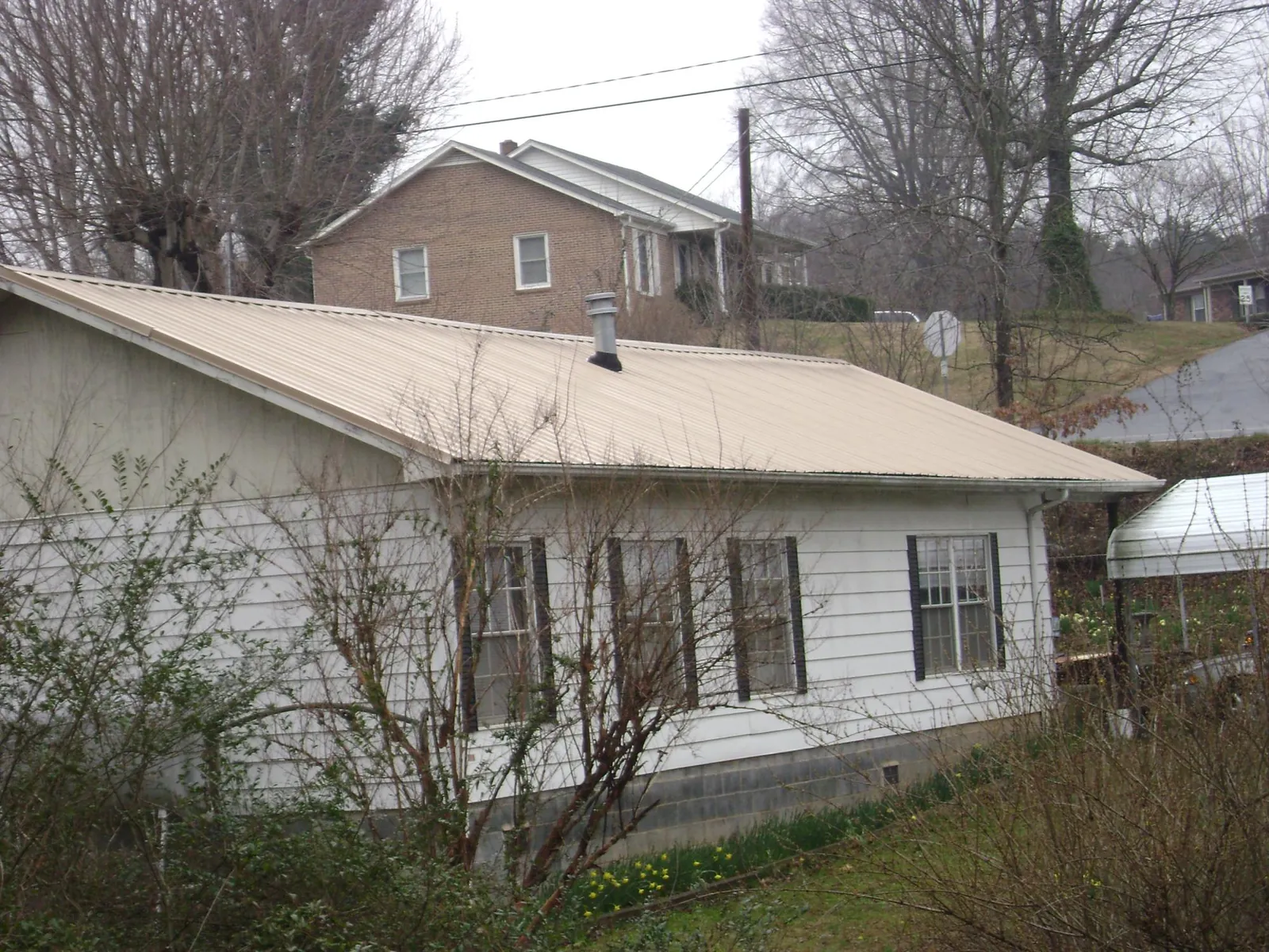 Tan metal roof on a white sided house set into a hillside — Commercial Roofing by Roofing Brothers in Tobyhanna