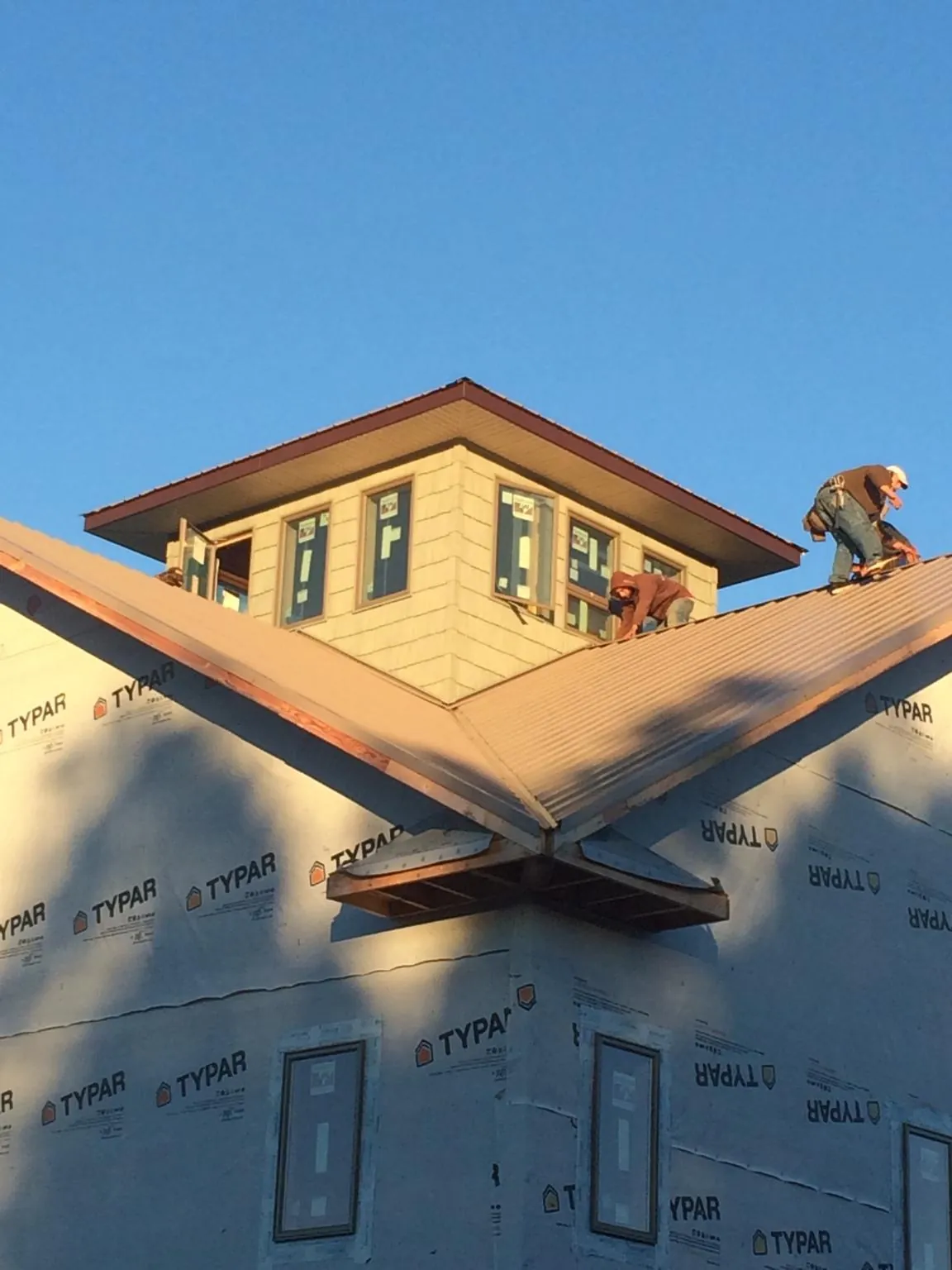 Roofers working around a rooftop cupola on a new metal roof at sunset — Roof Waterproofing in Tobyhanna by Roofing Brothers